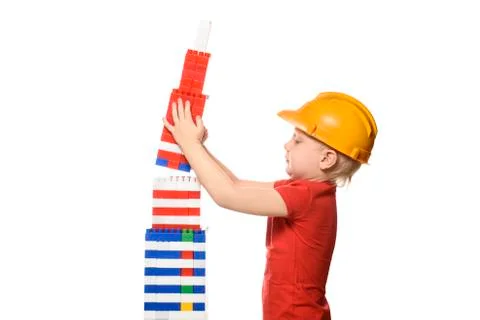 Blond boy in construction helmet and red t-shirt builds a skyscraper from the Stock-Fotos