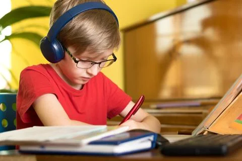 Blond boy does homework at the table in headphones Stock Photos