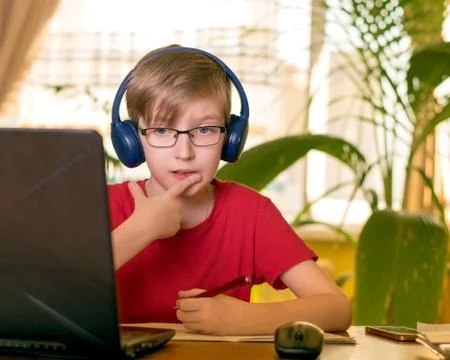 Blond boy does homework at the table in headphones Stock Photos