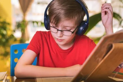 Blond boy does homework at the table in headphones Stock Photos
