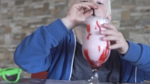 A blond boy is drinking a milk cocktail from a large stack Stock Footage 106872143