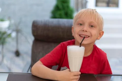 Blond boy is drinking milkshake and smiling. Child in cafe Stock-Fotos