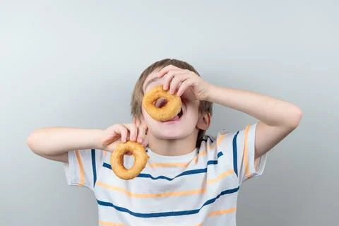 A blond boy eats donuts or crumpets. Stock Photos