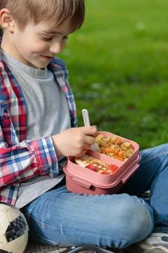 A blond boy eats lunch from a plastic container. Lunch in nature after training Stock Photos
