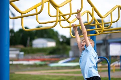 Blond boy hanging on monkey bars at outdoor playground Stock Photos