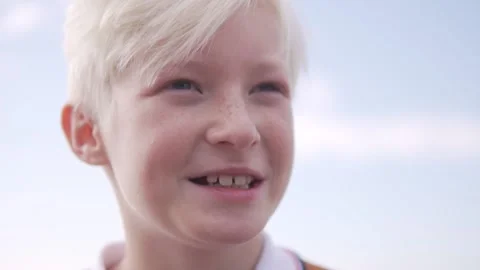 A blond boy looks at the camera against the sky and talks Video stock 224735507