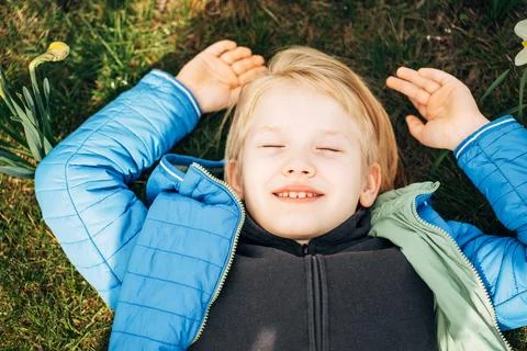 Blond boy lying in a daffodil field with a dreamy expression, enjoying the Stock Photos
