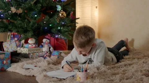 Blond boy lying under the christmas tree, and writing a letter to Santa 스톡 동영상 67720615
