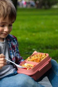 A blond boy in the park eats lunch from a lunch box. Close-up, portrait, meals Stock Photos