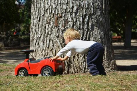 Blond boy playing with his red toy car Stock Photos