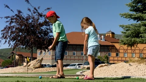 Blond boy putts the ball in the mini golfing yard Stock Footage 118703777