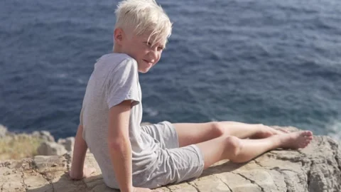 A blond boy sits on a cliff by the sea and enjoys the view Stock Footage 211806726