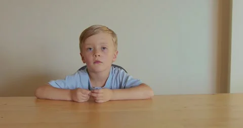 A blond boy sits thoughtfully and focused at a table. Children imagination Video stock 324819556