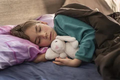 Blond boy sleeping in bed holding a toy Stock Photos
