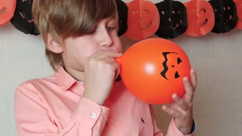 A blond boy smiling Inflating the orange balloon for Halloween at home Stock Footage 141039111