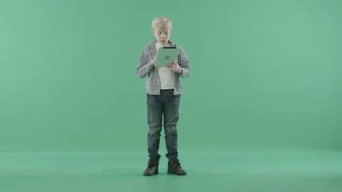 Blond boy standing on a green screen using his tablet computer Stock Footage 77718506