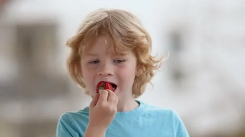 A blond boy on the street eats a ripe red strawberry 스톡 동영상 229794761