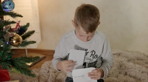Blond boy under christmas tree puts a letter to Santa in an envelope Stock-Footage 67728180