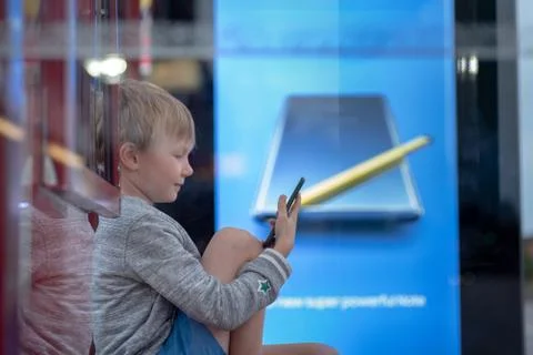 Blond boy using smartphone at the bus stop in UK Foto stock