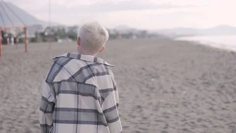 A blond boy walks along the beach by the sea on a cloudy day Stock Footage 224736919