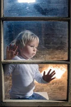 Blond child behind the window, looking outside Stock Photos
