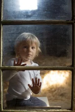 Blond child behind the window, looking outside Stock Photos