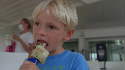 Blond child eats ice cream, he licks taste cold dessert with his tongue Stock Footage 194037850