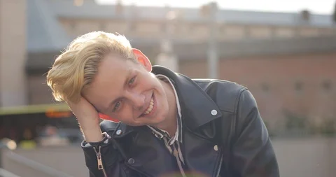 Blond guy in black jacket sits on the street. the sun shines bright. guy runs Stock Footage 126576374