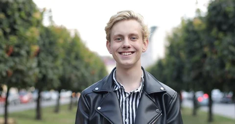 The blond guy stands in the park and is in a good mood. the guy feels happy. Video stock 126576619