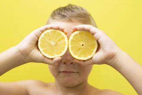 Blond-haired 7-year-old boy with two halves of natural lemons over his eyes Stock Photos