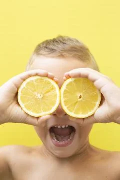 Blond-haired 7-year-old boy with two halves of natural lemons over his eyes Stock Photos
