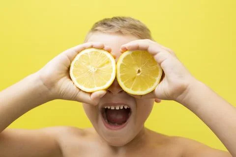 Blond-haired 7-year-old boy with two halves of natural lemons over his eyes Stock Photos