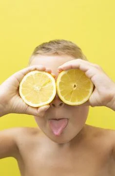 Blond-haired 7-year-old boy with two halves of natural lemons over his eyes Stock Photos