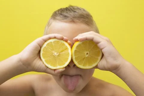 Blond-haired 7-year-old boy with two halves of natural lemons over his eyes Stock Photos