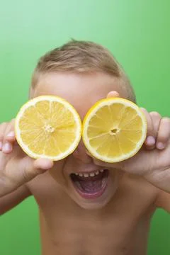Blond-haired 7-year-old boy with two lemons over his eyes screaming Stock Photos
