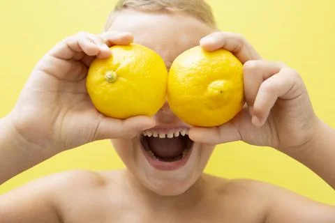 Blond-haired 7-year-old boy with two halves of natural lemons over his eyes Stock Photos