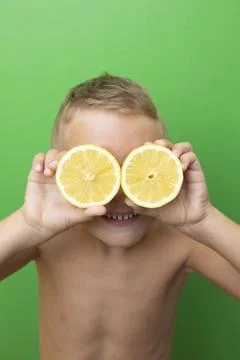 Blond-haired 7-year-old boy with two lemons over his eyes smiling Stock Photos