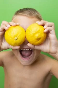 Blond-haired 7-year-old boy with two lemons over his eyes screaming Stock Photos