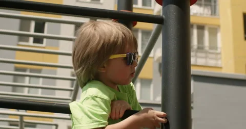 Blond kid in sunglasses has fun climbing on uneven bars Stock Footage 201487258