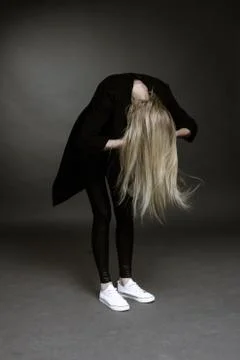 The blond leaned forward against the dark background. her hair covers her fac Stock Photos