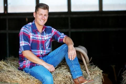 Blond man in jeans sitting on haystack Stock-Fotos