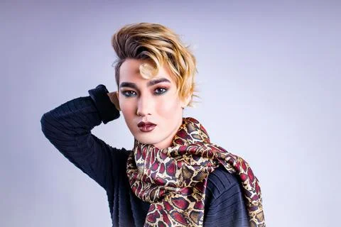 Blond man with make up on face posing in studio on white background Stock Photos