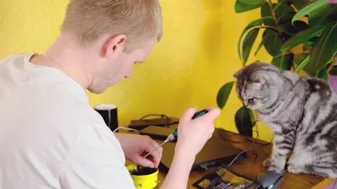 A blond man sits at a table with a screwdriver in his hands and fixes his watch. Stock Footage 150487529