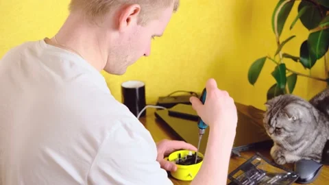 A blond man sits at a table with a screwdriver in his hands and fixes his watch. Stock Footage 150569785