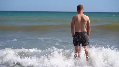 A blond man in swimming trunks stands on the beach Stock Footage 142399828
