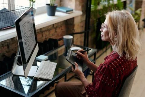 Blond mature mobile application developer sitting in front of computer monitor Stock Photos