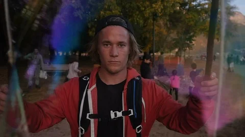 Blond men with cap bagpack create big bubble into the forest park with people Stock Footage 87518848