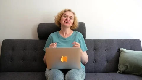 Blond middle-aged woman using laptop relaxing Sitting On Sofa At Home talki.. Stock Footage 246969701