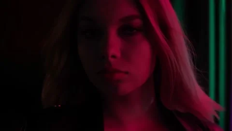 Blond model standing on a dark street in the neon-red lights of a sign Stock Footage 169924450
