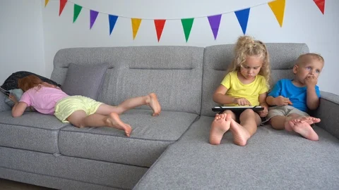 Blond sister with brother using tablet computer and redhead girl crying on sofa Stock Footage 122052074